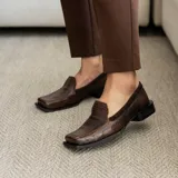 Mocasines negros de cuero con textura tipo reptil, punta cuadrada y detalle de aplique de cuero liso en el empeine.