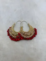Aros tipo argolla dorados con diseño calado de filigrana y colgantes de pequeñas cuentas rojas en el borde inferior.