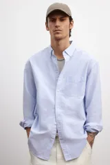 Camisa de vestir celeste y blanco a rayas verticales, de corte regular fit, con cuello abotonado, bolsillo en el pecho y mangas largas con puños abotonados.