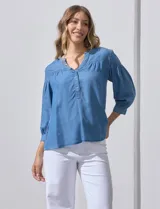 Blusa celeste de lyocell con cuello a la base y escote en V con apertura central y botones. Manga ¾ con puño y botón.