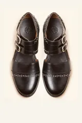 Zapato tipo monk strap con aberturas laterales, confeccionado en cuero vacuno color bordó. Presenta doble tira con hebillas metálicas plateadas en el empeine y suela de cuero con taco bajo.