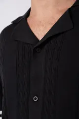 Camisa tejida color crudo, de manga corta, con cuello bowling y botones frontales. Presenta un tejido con textura de trenzas verticales y rib negro en los puños.