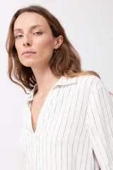 Blusa de lino a rayas verticales blancas y negras, con cuello camisero y mangas cortas.