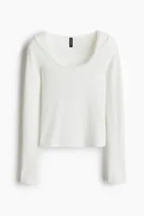 Remera blanca de manga larga, corte ajustado y corto (cropped), confeccionada en tejido acanalado. Presenta un escote pronunciado ribeteado en encaje y un pequeño moño de satén en el centro del escote.