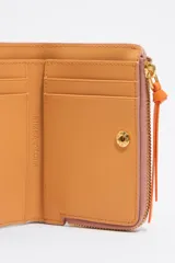 Monedero negro de piel con estructura rígida, logo metálico dorado, tirador de cordón y acabados metálicos dorados. Tarjetero interior, cierre con botón de presión e interior con logo grabado. Confeccionada en 100% poliéster reciclado y 100% poliuretano de producción responsable.