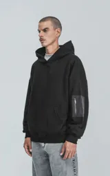 Hoodie negro de corte oversize con capucha, bolsillo tipo canguro y detalle de bolsillo con cierre en la manga izquierda.