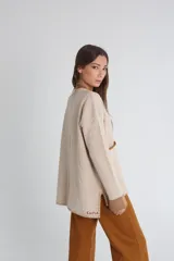 Saco cardigan beige de tejido de punto acanalado con cuello en V, cierre frontal con botones marrones, bolsillos de parche y ribete marrón en cuello, bolsillos y puños.