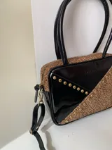 Cartera rígida negra de cuero con tachas plateadas y tres combinaciones de cuero diferentes que aportan textura. Tiene herrajes y cierre metálico plateado marca YKK. Cuenta con un asa fina para llevar al hombro o en la mano y una correa larga extra regulable.