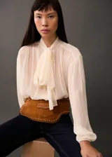 Blusa color crema de mangas largas abullonadas, con lazo en el cuello y tejido semitransparente.