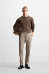 Pantalón color arena de corte recto, confeccionado en tejido elástico. Cuenta con cintura elástica ajustable con cordón, bolsillos laterales y bolsillos de vivo en la parte trasera.