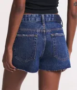 Short de jean azul oscuro, de tiro alto, con bolsillos delanteros y traseros, cierre con botón y cremallera, trabillas dobles y terminación deshilachada.