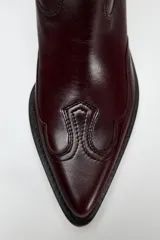 Bota de cuero color bordó, estilo cowboy, con puntera marcada y tiradores laterales.