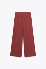 Pantalón color ladrillo de tiro medio con trabillas, detalle de pliegues, bolsillos laterales y falsos bolsillos de vivo en la espalda. Cierre frontal con cremallera y botón.