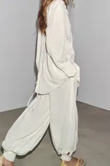 Pantalón de tiro medio color crudo con rayas verticales, confeccionado en hilatura con lino. Tiene bolsillos laterales ocultos en costura y de vivo en espalda, detalle de pliegues y bajo acabado en puño.