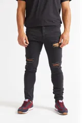 Jean skinny de hombre color negro, ajustado desde la cadera hasta los tobillos, con roturas en las rodillas y logo bordado en el bolsillo trasero.
