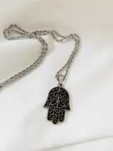 Cadena con dije en acero quirúrgico en forma de mano de Fátima, con detalles en blanco.