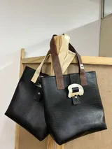 Bolso tipo tote bag negro con textura símil cuero de cocodrilo, doble asa corta de cuero marrón y beige, y cierre con broche metálico con forma orgánica.