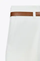 Pantalón marrón de tiro alto con cinturón negro, bolsillos delanteros y cierre frontal con cremallera y gancho metálico.