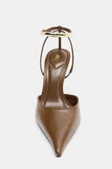 Zapato de tacón alto fino, color marrón, con punta afilada y escote redondo. Presenta una pulsera al tobillo con hebilla y detalle metálico dorado.