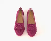 Mocasín de cuero gamuzado color fucsia, con flecos en la capellada y un lazo con herrajes metálicos dorados. Interior forrado en cuero y suela de goma flexible.