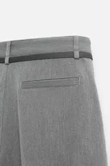 Pantalón gris de corte ancho con pliegues frontales y cinturón fino negro.