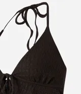 Blusa marrón oscuro con textura plisada, estilo frente única (halter) con escote en V profundo y lazo ajustable en el centro del busto. Presenta un ruedo con volado o efecto nube.