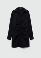 Minivestido camisero negro con finas rayas verticales blancas, de manga larga con puños abotonados, cuello camisero y cierre frontal con cremallera. Presenta frunces verticales en el frente.