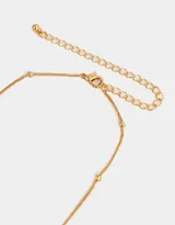 Collar corto dorado con cadena de eslabones y dijes colgantes: cerezas, moño, trébol de cuatro hojas, herradura, candado de corazón, manzana mordida y hongo rojo con lunares blancos.