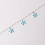 Tobillera dorada con cadena de eslabones y tres dijes de flores de resina celeste con un strass en el centro.