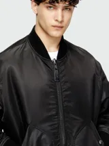 Campera bomber negra de hombre, estilo aviador, con cuello y puños acanalados. Presenta cierres metálicos visibles y bolsillos frontales con solapa y broche.