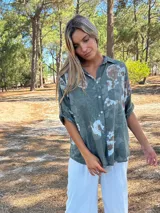 Camisa de algodón color verde militar con estampado floral en tonos claros. Presenta cuello camisero, botones frontales y mangas largas que se pueden remangar.