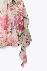 Vestido corto con estampado floral en tonos rosa y verde, escote fluido, tirantes finos y volantes en el lateral.