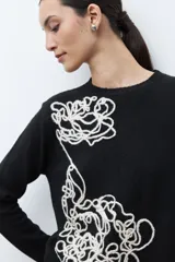 Sweater color rosado melange con cuello redondo y manga larga. Presenta un bordado abstracto en color crema en la parte frontal.