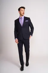 Ambo de vestir azul marino, corte slim fit, compuesto por saco de dos botones con solapa de muesca, dos bolsillos delanteros con solapa y un bolsillo en el pecho, y pantalón de vestir con bolsillos laterales y traseros. Incluye camisa lila, corbata y pañuelo de bolsillo al tono.