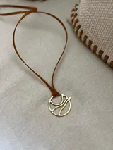 Gargantilla marrón con dije circular dorado con diseño abstracto.