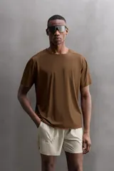 Camiseta deportiva marrón confeccionada en tejido técnico ligero y elástico con estructura perforada. Cuello redondo, manga corta y bajo asimétrico con aberturas laterales. Detalle de logo estampado.