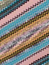 Capa tipo poncho de tejido de punto con diseño de zigzag multicolor en tonos amarillo, gris, negro y beige. Presenta cuello en V y flecos en el borde inferior.