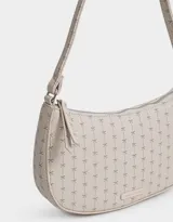 Bandolera tipo baguette color crema con estampado de moños en gris. Tiene asa corta para llevar al hombro, cierre superior y tag metálico con logo.