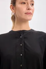 Vestido corto negro con cuello mao, abotonadura parcial y mangas largas abullonadas.