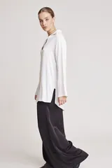 Camisa blanca de satén con cuello clásico, cierre frontal con botones y mangas largas.