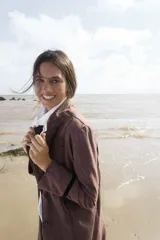 Tapado largo color marrón oscuro, con solapas anchas y cierre frontal de un solo botón. Presenta un detalle de cinta negra en la manga.