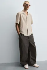 Pantalón cargo de corte ancho y relajado, color verde oscuro o negro, con cintura elástica, bolsillos laterales de parche y bolsillos traseros de vivo. Presenta pliegues verticales marcados en la parte delantera y cordones ajustables en los bajos.