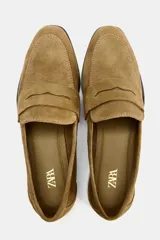 Zapato plano tipo mocasín color marrón claro, confeccionado en piel de serraje. Tiene copete subido, antifaz y punta redonda.
