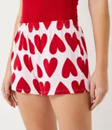 Conjunto de pijama short doll de algodón, compuesto por un top rojo con tirantes finos y encaje en el escote, y un short blanco con estampado de corazones rojos.