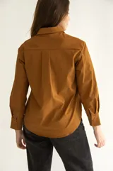Camisa marrón de corte clásico, con cuello, mangas largas con puños abotonados, cierre frontal con botones al tono, bolsillo de parche en el pecho y ruedo redondeado.
