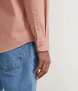 Camisa overshirt color salmón de sarga de algodón con capucha gris ajustable con cordones. Tiene cierre frontal con botones, dos bolsillos con solapa en el pecho y mangas largas con puños abotonados.