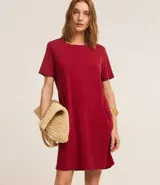 Vestido corto marrón, estilo camiseta, con escote redondo, mangas cortas y bolsillos laterales. El bajo es redondeado.