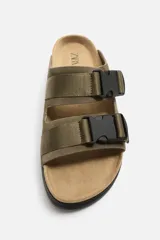 Sandalias planas color beige con doble tira ancha en el empeine y cierre con hebilla.