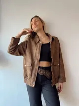 Campera marrón de gamuza con cuello clásico, cierre frontal con cremallera y bolsillos con solapa y botón.