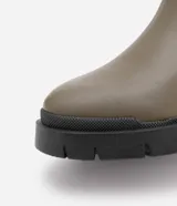 Bota Chelsea color verde oliva, confeccionada en cuero sintético, con laterales elásticos negros y suela track negra.
